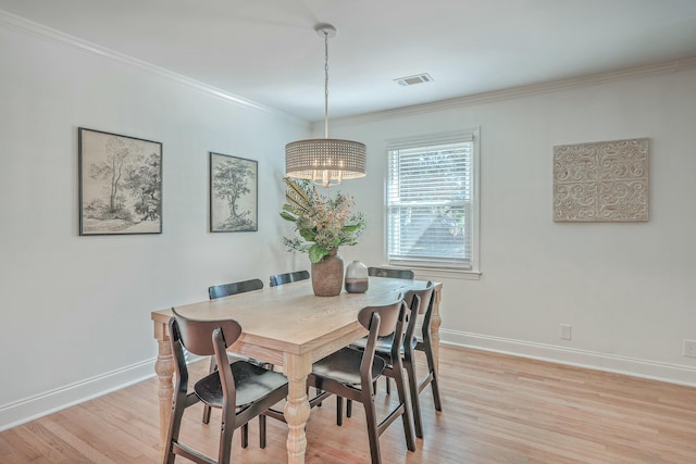 dining room featuring crown molding, light wood-type flooring, and a notable chandelier