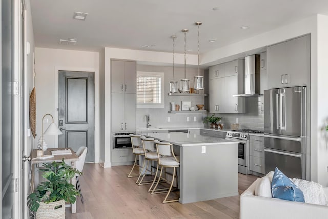 kitchen with a kitchen island, appliances with stainless steel finishes, backsplash, a kitchen bar, and wall chimney exhaust hood