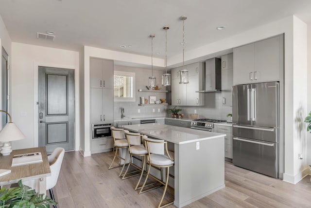 kitchen featuring light hardwood / wood-style flooring, a breakfast bar, stainless steel appliances, a kitchen island, and wall chimney exhaust hood