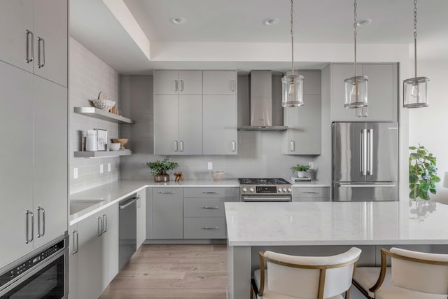 kitchen featuring a kitchen bar, tasteful backsplash, pendant lighting, stainless steel appliances, and wall chimney range hood