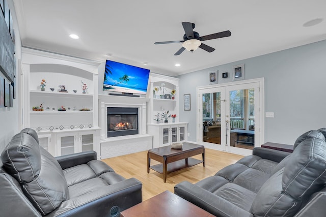 living room featuring crown molding, ceiling fan, light hardwood / wood-style floors, built in shelves, and french doors