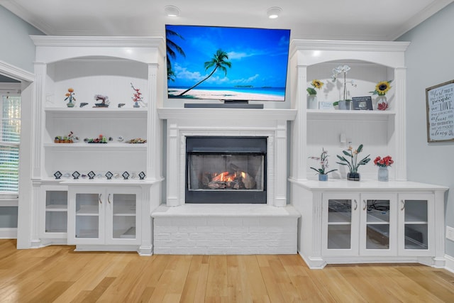 unfurnished living room with hardwood / wood-style flooring, a fireplace, built in shelves, and crown molding