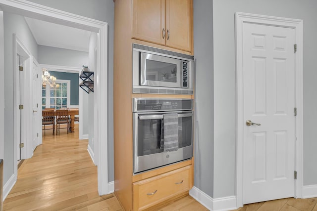 kitchen with light brown cabinetry, a notable chandelier, stainless steel appliances, and light hardwood / wood-style floors