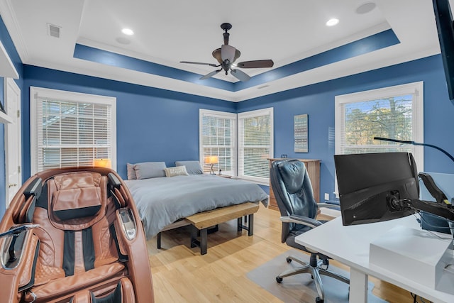 bedroom with multiple windows, a raised ceiling, and light wood-type flooring