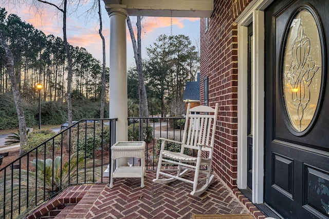 balcony at dusk featuring covered porch