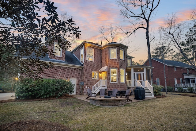 back house at dusk with a sunroom, a lawn, and a patio area