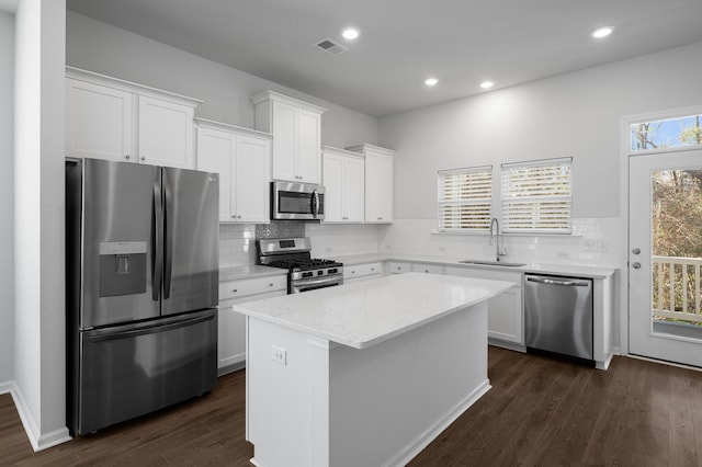 kitchen featuring appliances with stainless steel finishes, a center island, light stone counters, sink, and white cabinetry