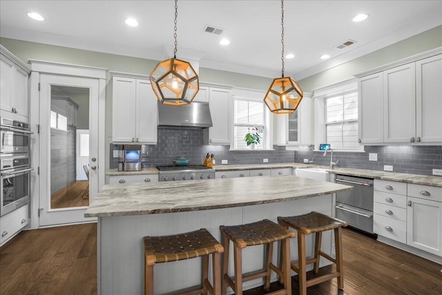 kitchen featuring under cabinet range hood, visible vents, a kitchen breakfast bar, and a sink