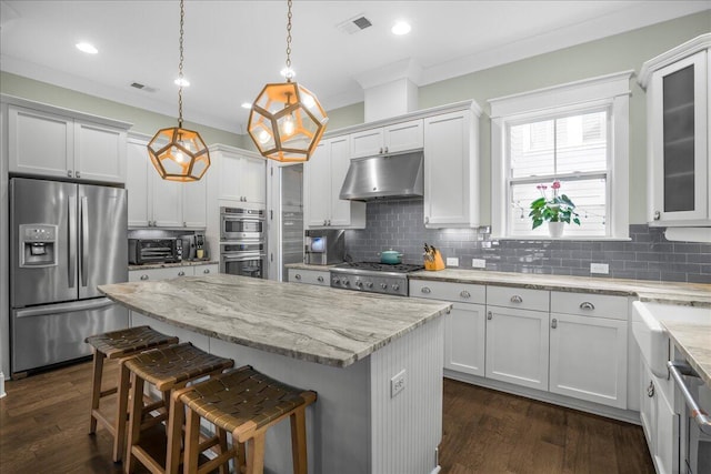 kitchen featuring backsplash, a kitchen island, under cabinet range hood, a kitchen breakfast bar, and stainless steel appliances