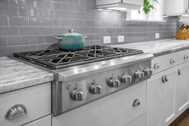 room details with decorative backsplash, white cabinets, light stone countertops, and stainless steel gas cooktop