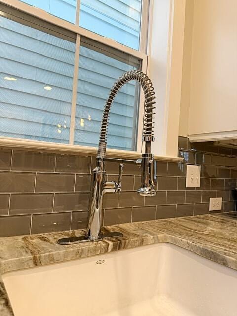 room details featuring backsplash, white cabinets, stone countertops, and a sink