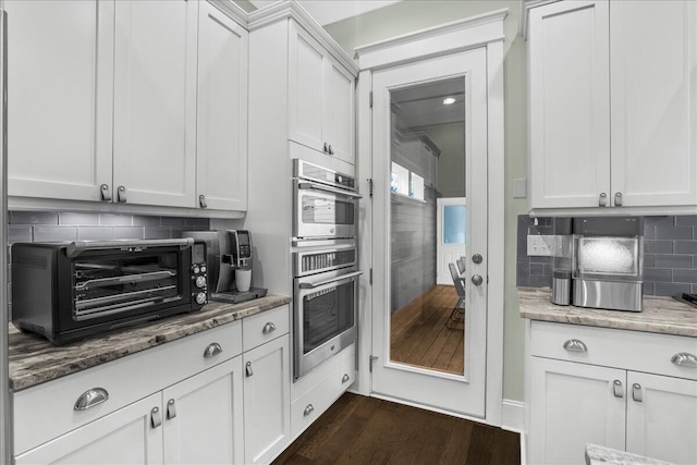 kitchen featuring light stone countertops, a toaster, dark wood-style floors, stainless steel double oven, and white cabinets