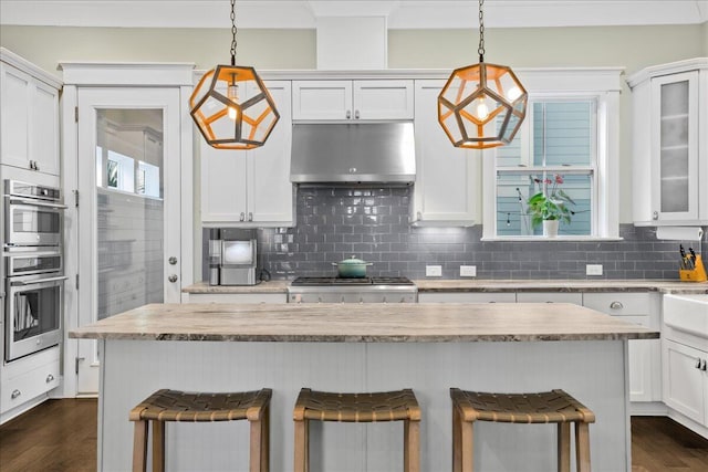 kitchen with under cabinet range hood, decorative backsplash, a kitchen breakfast bar, stainless steel double oven, and white cabinetry