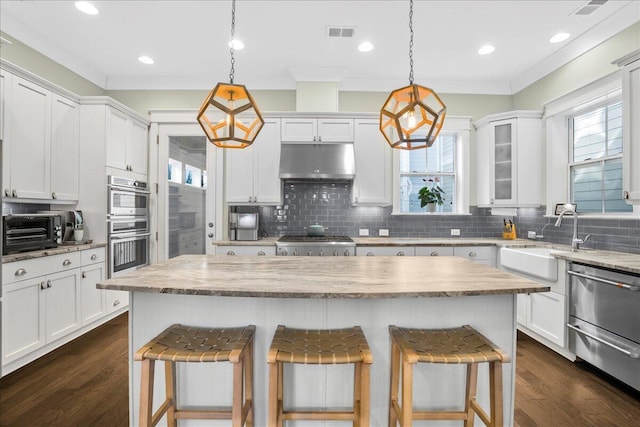 kitchen with visible vents, under cabinet range hood, a kitchen bar, appliances with stainless steel finishes, and a sink