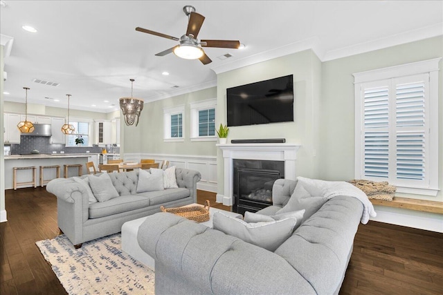 living area with dark wood finished floors, visible vents, crown molding, and a ceiling fan