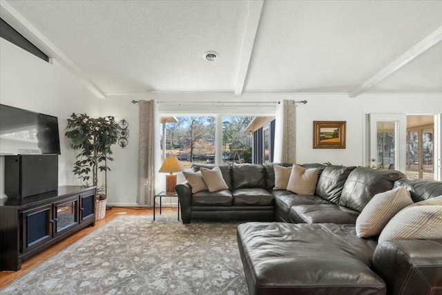 living room with lofted ceiling with beams, light wood-type flooring, and a textured ceiling