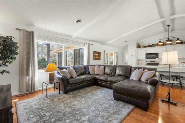 living room with light hardwood / wood-style floors, a textured ceiling, and vaulted ceiling with beams