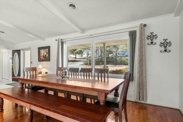 dining space featuring beamed ceiling, wood-type flooring, and a textured ceiling