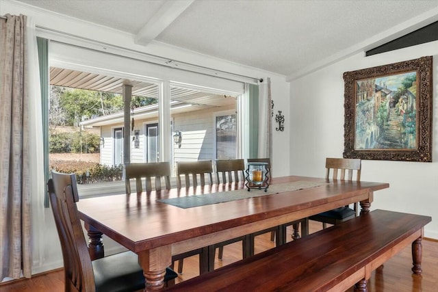 dining space featuring hardwood / wood-style floors, a textured ceiling, and vaulted ceiling with beams