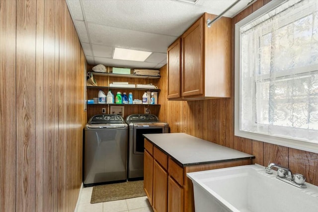 laundry room featuring wooden walls, sink, cabinets, light tile patterned floors, and independent washer and dryer