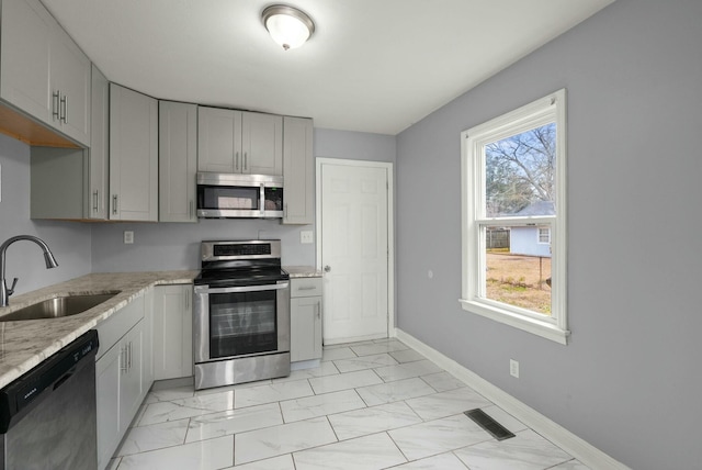 kitchen with stainless steel appliances, sink, light stone counters, and gray cabinets