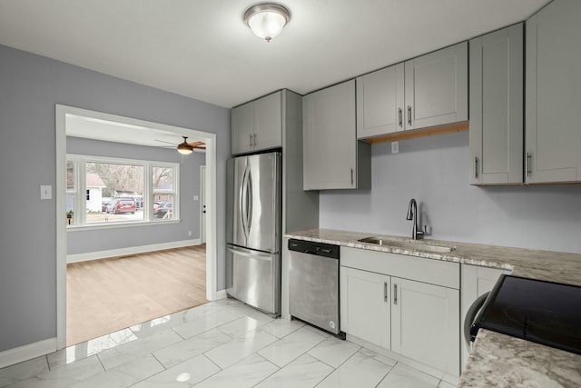 kitchen with light stone countertops, stainless steel appliances, gray cabinets, ceiling fan, and sink