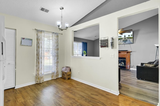 dining area featuring visible vents, a fireplace with flush hearth, wood finished floors, baseboards, and vaulted ceiling