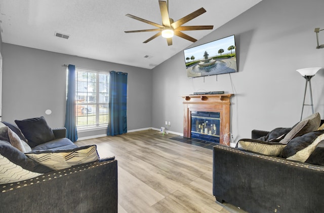 living area featuring visible vents, baseboards, a fireplace with flush hearth, vaulted ceiling, and wood finished floors