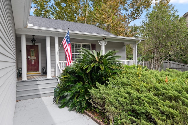 entrance to property with covered porch, roof with shingles, and fence