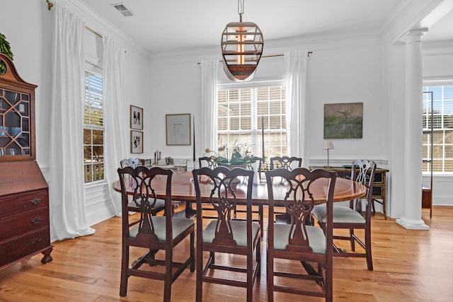 dining space with an inviting chandelier, crown molding, ornate columns, and light hardwood / wood-style flooring