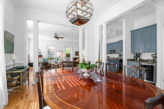 dining room with light hardwood / wood-style floors, decorative columns, ornamental molding, ceiling fan, and wine cooler