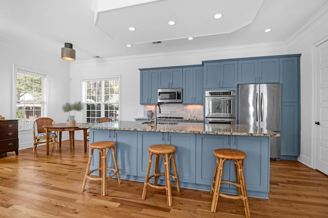 kitchen with appliances with stainless steel finishes, a large island with sink, light hardwood / wood-style floors, and stone countertops