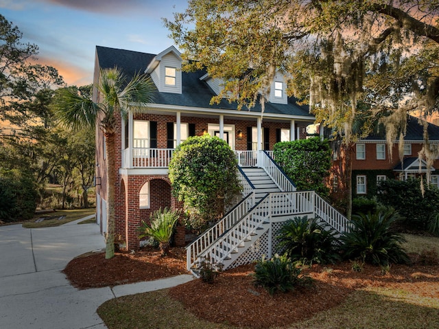 view of front facade with stairway, brick siding, a porch, and concrete driveway