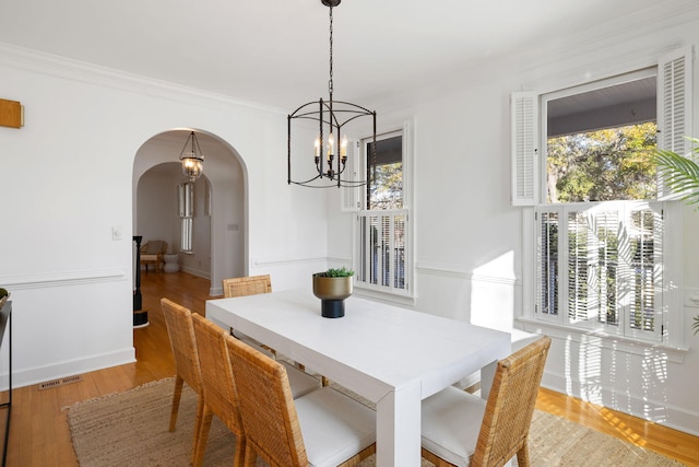 dining space with arched walkways, plenty of natural light, ornamental molding, and wood finished floors