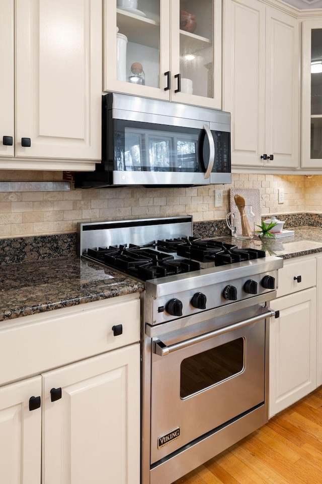 kitchen featuring dark stone countertops, backsplash, appliances with stainless steel finishes, and light wood-style flooring