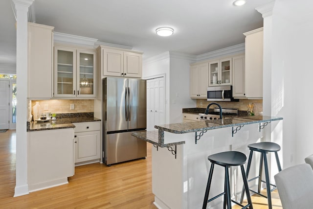 kitchen featuring a kitchen bar, ornamental molding, a peninsula, light wood-style floors, and stainless steel appliances