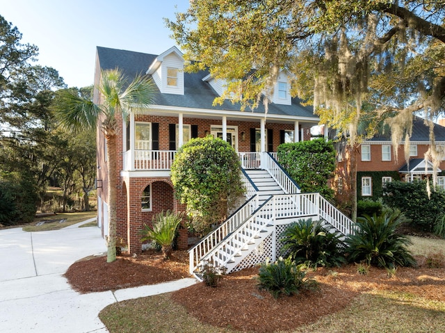 view of front of home with brick siding, covered porch, concrete driveway, and stairs