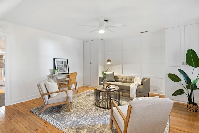 living area featuring a decorative wall, visible vents, a ceiling fan, and light wood finished floors