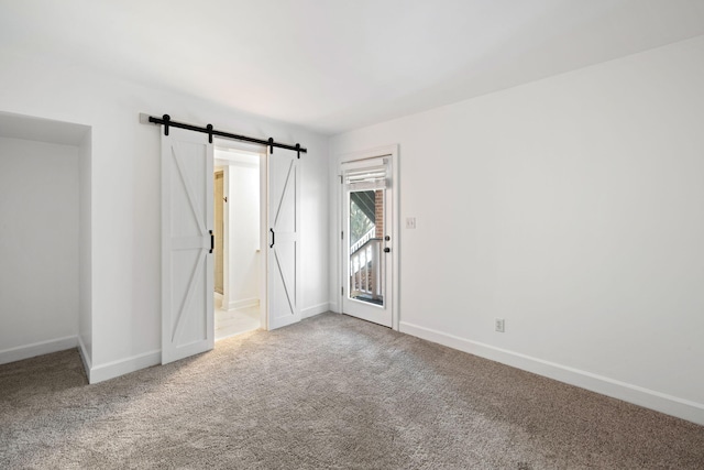 carpeted spare room featuring a barn door and baseboards