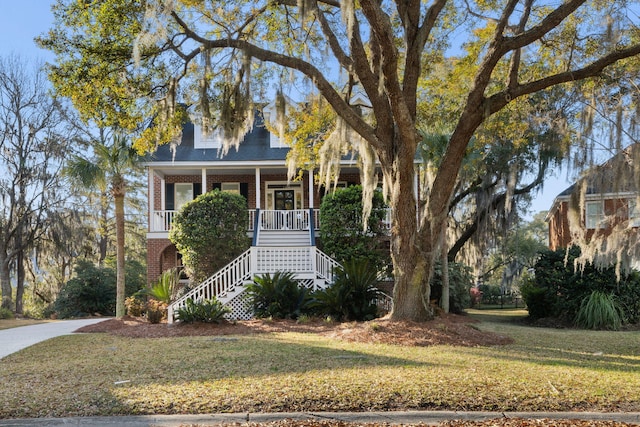 view of front of house featuring stairs, brick siding, covered porch, and a front yard