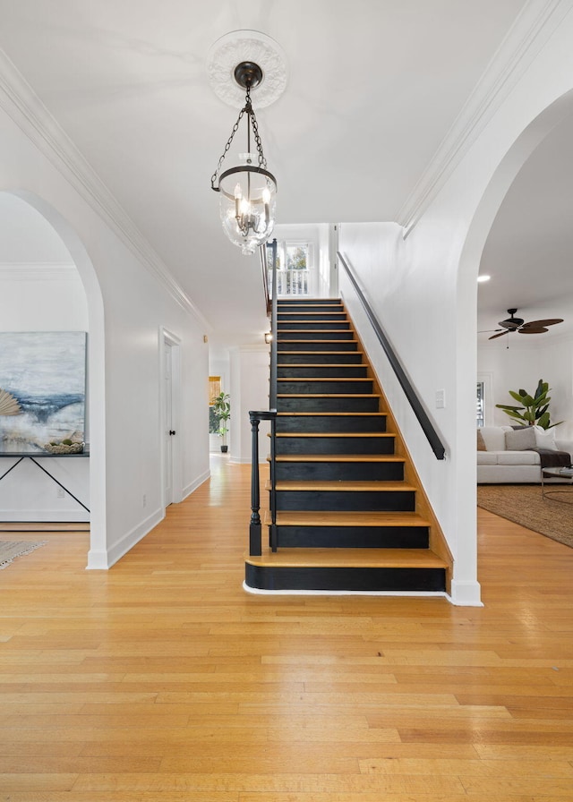 staircase with baseboards, arched walkways, wood finished floors, and ornamental molding