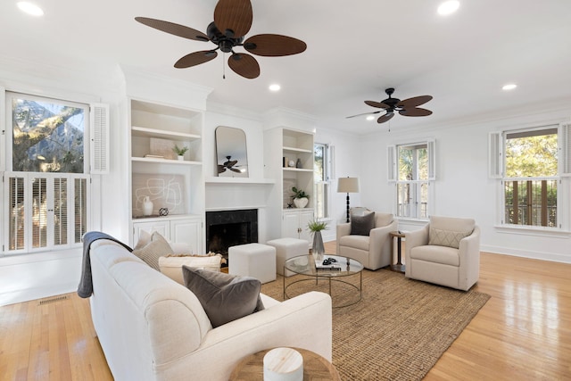 living room featuring baseboards, a premium fireplace, recessed lighting, light wood-style floors, and crown molding