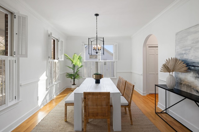 dining room with baseboards, arched walkways, light wood finished floors, and ornamental molding