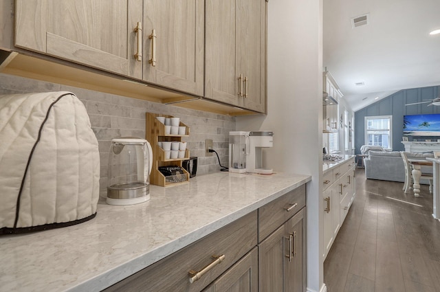 kitchen featuring dark hardwood / wood-style floors, stainless steel gas stovetop, vaulted ceiling, light stone counters, and backsplash