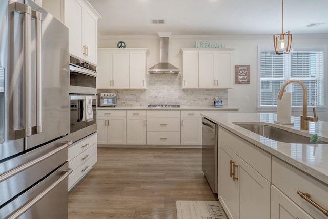 kitchen with tasteful backsplash, light wood-type flooring, wall chimney exhaust hood, sink, and appliances with stainless steel finishes