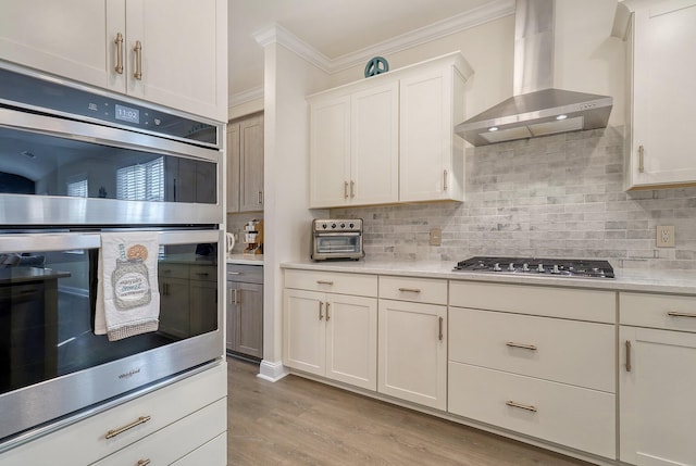 kitchen featuring stainless steel appliances, light wood-type flooring, backsplash, wall chimney range hood, and ornamental molding