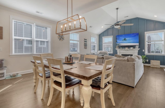 dining space featuring a premium fireplace, ceiling fan with notable chandelier, vaulted ceiling, and hardwood / wood-style flooring