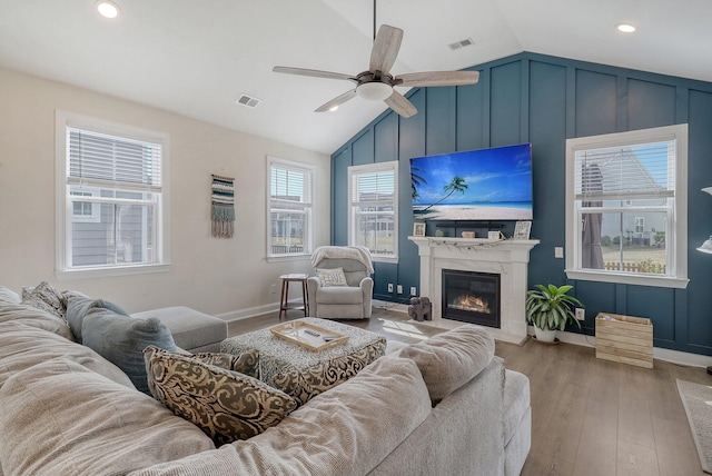 living room featuring ceiling fan, vaulted ceiling, wood-type flooring, a premium fireplace, and a wealth of natural light