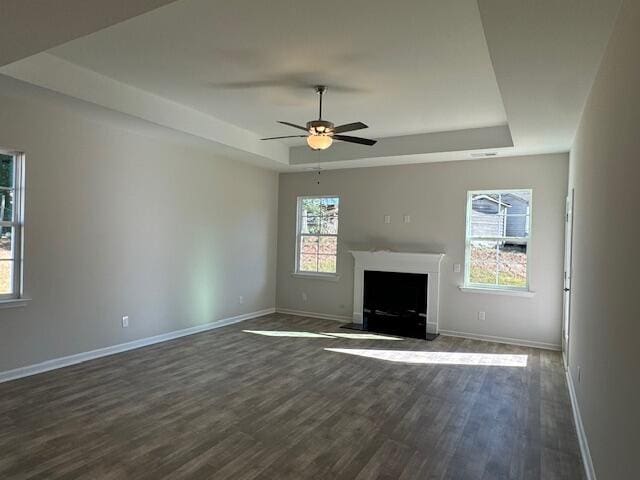 unfurnished living room with dark hardwood / wood-style floors, a raised ceiling, ceiling fan, and a healthy amount of sunlight