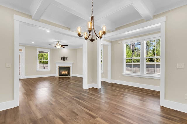 unfurnished living room featuring dark wood-type flooring, beam ceiling, ornamental molding, a fireplace, and ceiling fan with notable chandelier